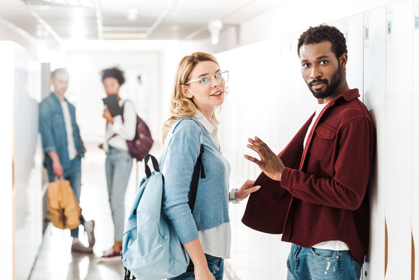 smiling multiethnic students standing in corridor in college - 写真・画像