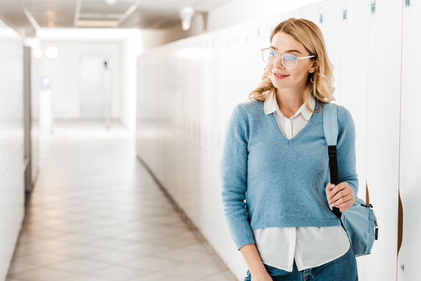 smiling student in glasses with backpack in corridor in college - Fotó, kép
