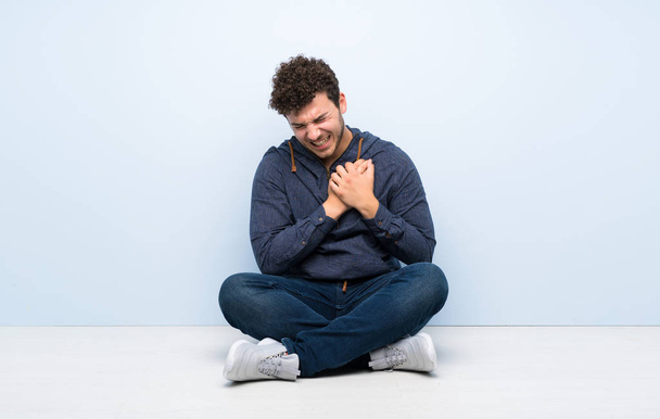 Young man sitting on the floor having a pain in the heart - Foto, afbeelding