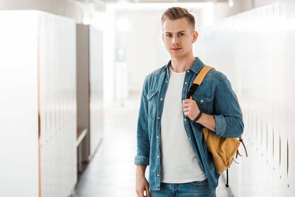 student with backpack looking at camera in corridor in university - Photo, Image