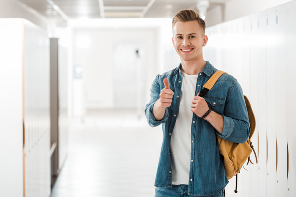 student with backpack showing thumb up in corridor in university - Fotó, kép