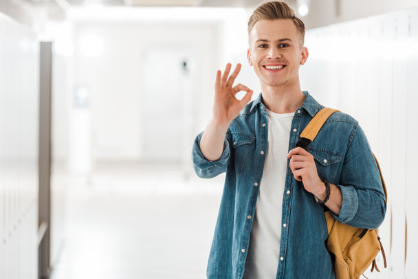 student with backpack showing okay sign in corridor in university - Photo, Image