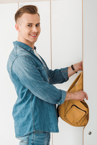 sorrindo estudante colocando mochila no armário e olhando para a câmera
 - Foto, Imagem