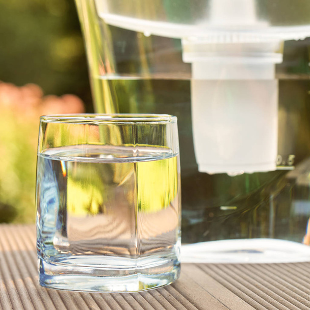 Wasserfilterkrug und ein sauberes Glas klaren Wassers aus nächster Nähe auf dem Hintergrund des Sommergartens - Foto, Bild