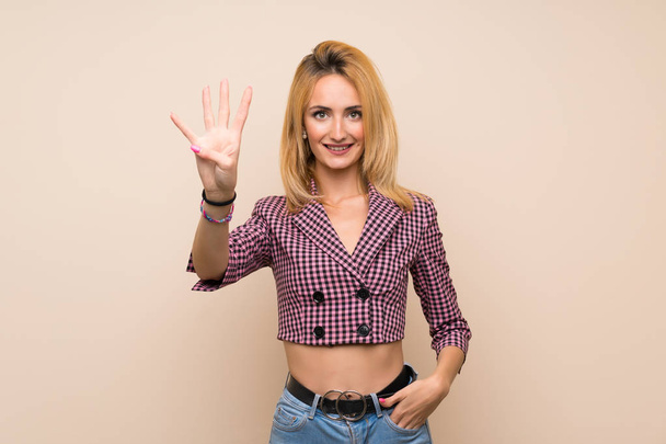 Młoda blondynka w różowej kurtce na odizolowanej ścianie szczęśliwa i licząca cztery palce - Zdjęcie, obraz
