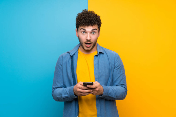 Man with curly hair over colorful wall surprised and sending a message - Foto, imagen