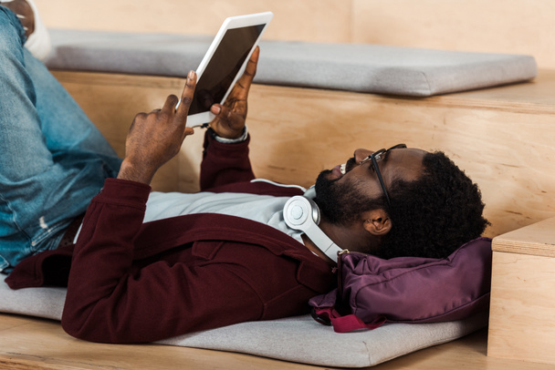 african american student  lying on backpack and using digital tablet in university - Φωτογραφία, εικόνα