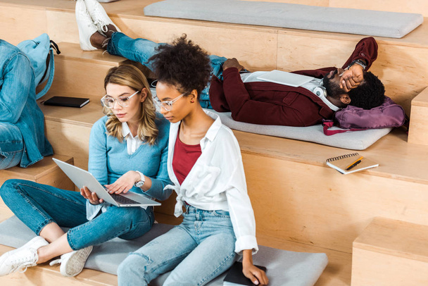 multiculturele studenten in glazen met laptop in collegezaal - Foto, afbeelding