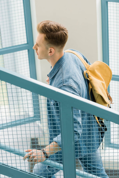 student in denim shirt with yellow backpack on stairs in university - Foto, Bild
