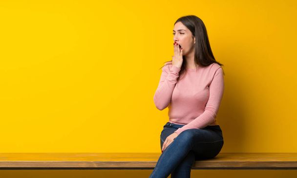 Mujer joven sentada en la mesa bostezando y cubriendo la boca abierta con la mano
 - Foto, Imagen