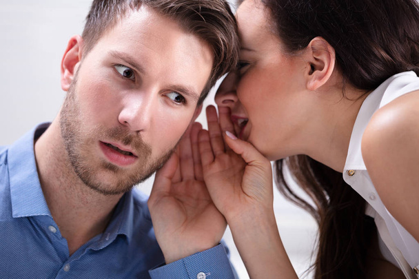 Close-up Of Young Businesswoman Whispering Into Male Partner's Ear - 写真・画像