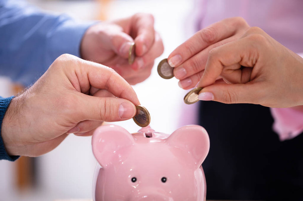 Strony biznesmenów Wstawianie monet w Pink Piggybank w biurze - Zdjęcie, obraz