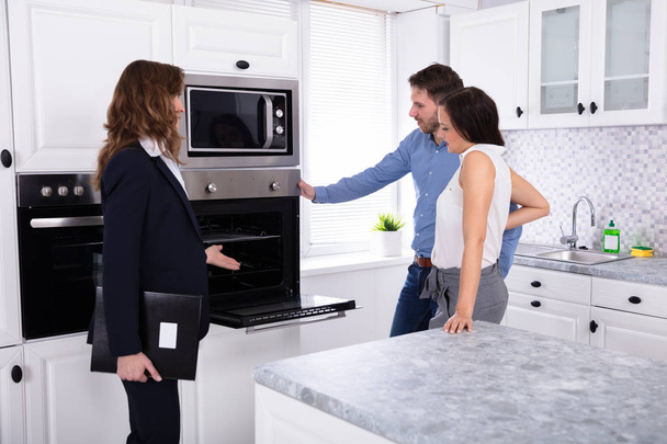 Real Estate Agent Showing Microwave Oven In House To A Young Couple - Photo, image