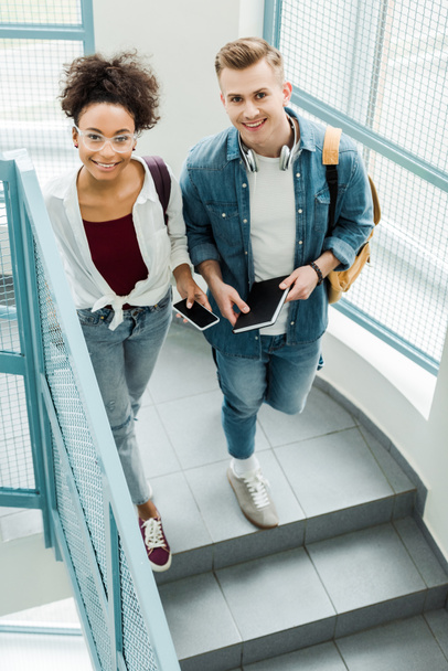 overhead view of two students with notebook and smartphone standing on stairs - Fotoğraf, Görsel