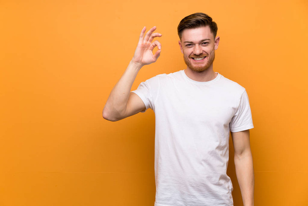 Redhead man over brown wall showing ok sign with fingers - Photo, Image