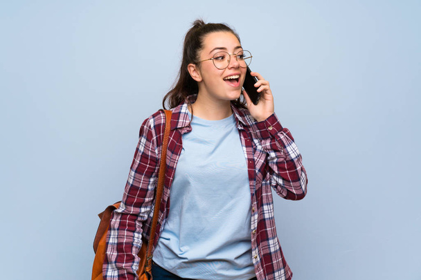 Έφηβος μαθητής κορίτσι πάνω από απομονωμένο μπλε τοίχο κρατώντας μια συνομιλία με το κινητό τηλέφωνο - Φωτογραφία, εικόνα