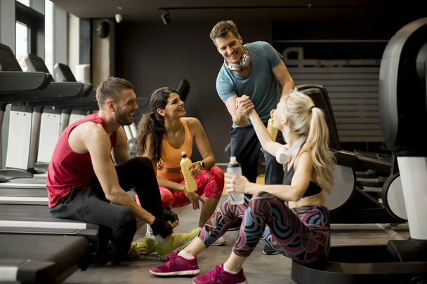 Groupe de jeunes en vêtements de sport parlant et riant ensemble assis sur le sol d'une salle de gym après une séance d'entraînement
 - Photo, image