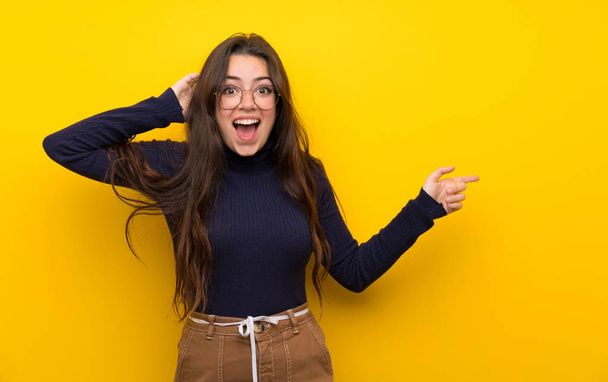 Teenager girl over isolated yellow wall surprised and pointing finger to the side - Foto, immagini