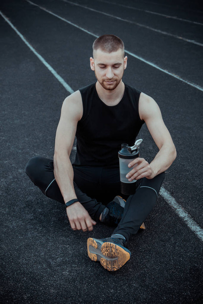 muscular slender man in training at the stadium drinks water from a sports shaker. recreation sports. athletic exercising - Photo, image