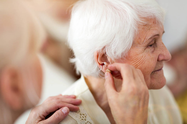 Vrouwelijke arts die gehoorapparaat toepast op het oor van de Senior vrouw - Foto, afbeelding