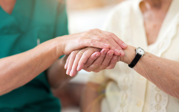 Νοσοκόμα παρηγορώντας τον ηλικιωμένο ασθενή της κρατώντας τα χέρια της - Φωτογραφία, εικόνα