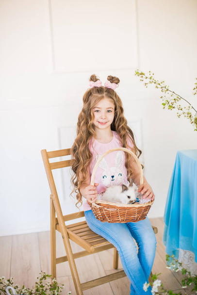 Little cute girl with long curly hair with little bunnies and Easter decor at home at the holiday table. - Photo, image
