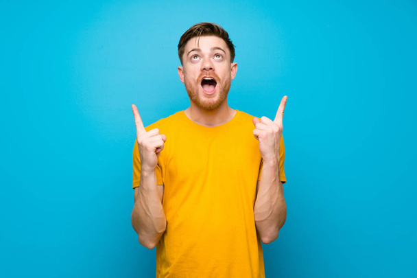 Redhead man over blue wall surprised and pointing up - Foto, immagini