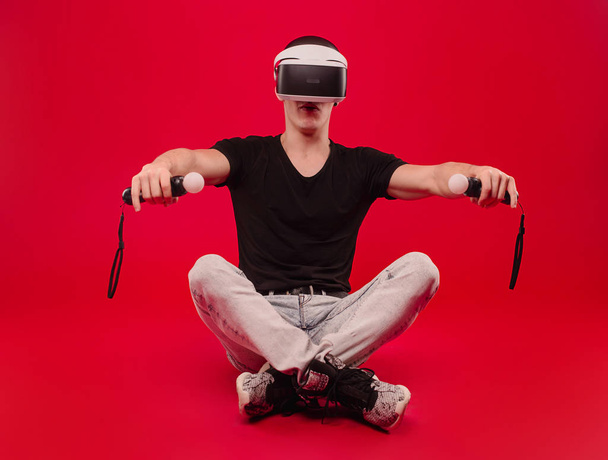 Ο άνθρωπος με γένια σε VR γυαλιά οδήγηση ποδήλατο, κόκκινο φόντο. Εικονική μαθήματα οδήγησης έννοια. Χίπστερ με αυτοπεποίθηση πρόσωπο οδήγηση αυτοκίνητο στην εικονική πραγματικότητα με σύγχρονο ψηφιακό gadget. - Φωτογραφία, εικόνα