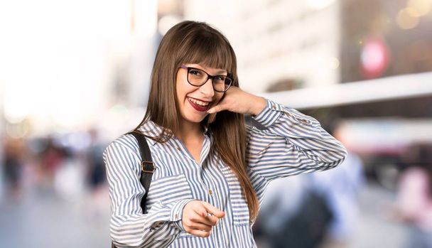 Woman with glasses making phone gesture and pointing front at outdoors - Photo, Image