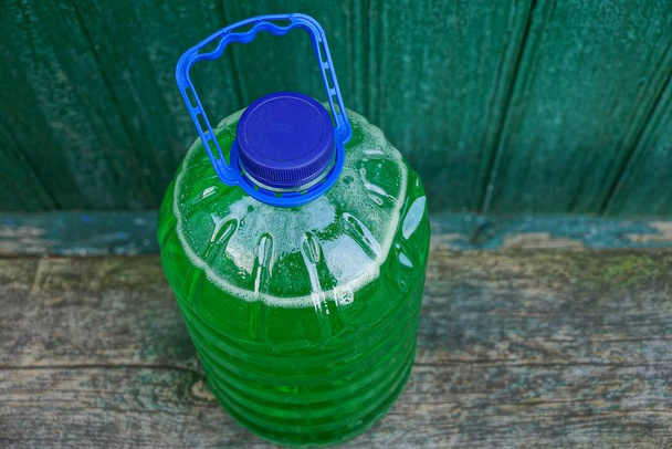 Grande garrafa de plástico com líquido verde em uma placa de madeira
 - Foto, Imagem
