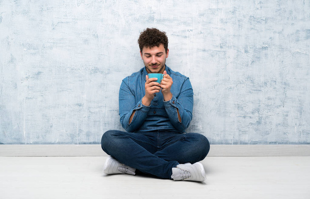 Young man sitting on the floor holding hot cup of coffee - Photo, Image