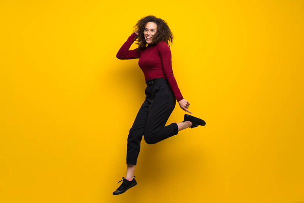 Dominican woman with curly hair jumping over isolated yellow wal - Photo, Image