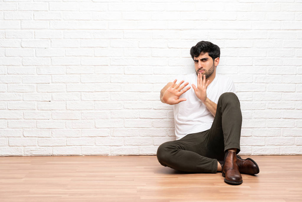 Jonge man zittend op de vloer nerveus stretching handen naar de voorkant - Foto, afbeelding