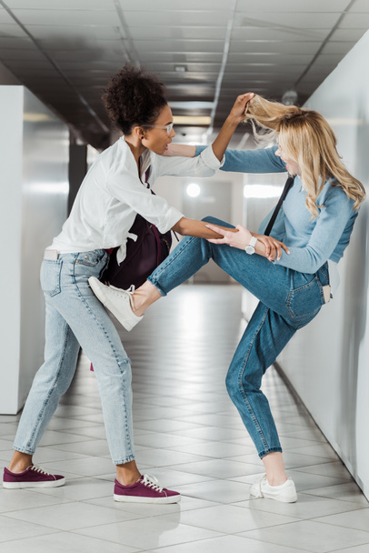 two students in jeans fighting in corridor in college - Фото, изображение