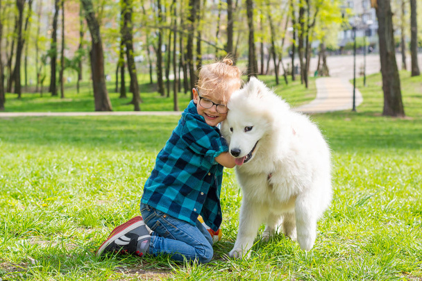 Kis csípő fiú szemüveg ölelgetés fehér bolyhos Szamojéd kutya egy - Fotó, kép