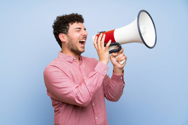 Man with curly hair over isolated blue wall shouting through a megaphone - Foto, Imagem