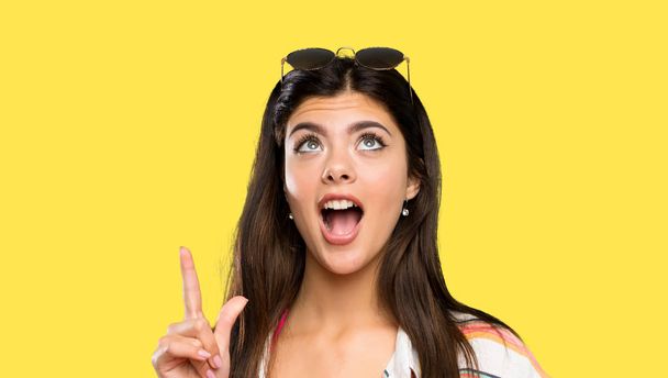 Teenager girl on summer vacation pointing with the index finger a great idea over isolated yellow background - Foto, Imagen