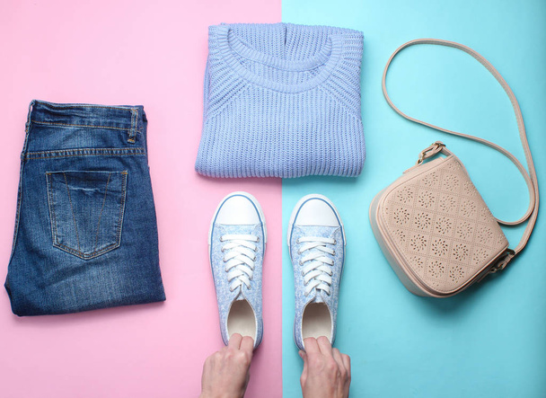 Women's accessories, clothing shoes on a pastel background. Jeans, sweater, bag. Women's hands hold sneakers. Creative flat lay. Top view. minimalism  - Foto, Imagem