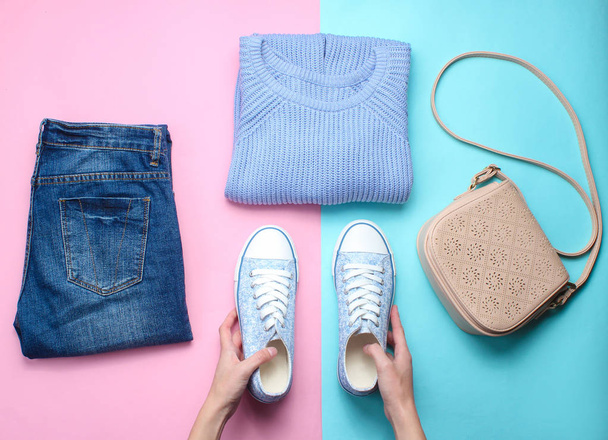 Women's accessories, clothing shoes on a pastel background. Jeans, sweater, bag. Women's hands hold sneakers. Creative flat lay. Top view. minimalism  - Photo, Image