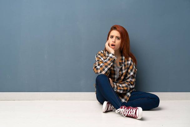 Young redhead woman sitting on floor surprised and shocked while looking right - Фото, зображення