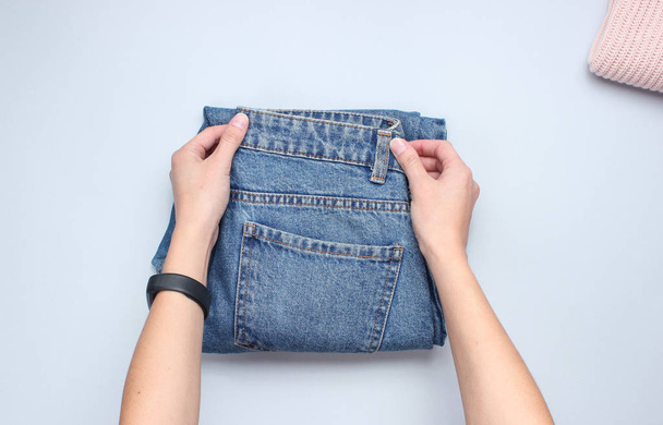 Hands fold jeans on a gray background. Conceptual photo. Top view - Zdjęcie, obraz