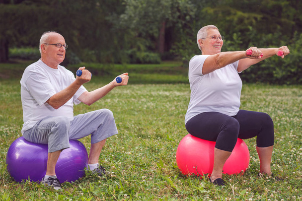 старшая спортивная пара сидит на фитнес-мяч с гантелями
 - Фото, изображение