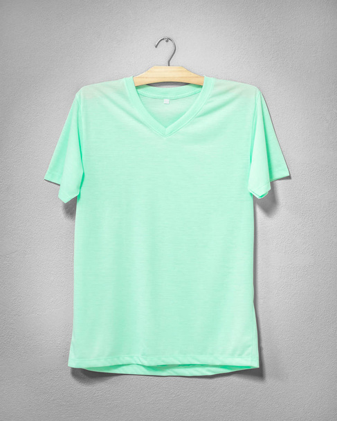 Green shirt hanging on cement wall. Empty clothing for design. Front view. - Photo, Image
