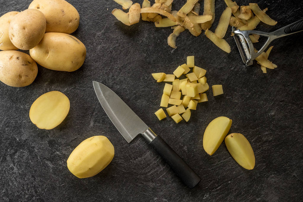 Knife cutting potatoes on textured black background. - Photo, Image