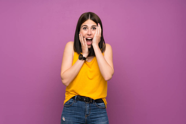 Jonge vrouw over geïsoleerde paarse muur met verrassing en geschokt gezicht uitdrukking - Foto, afbeelding