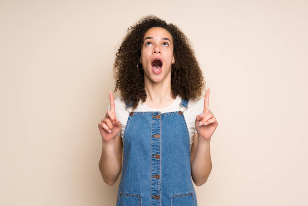Dominican woman with overalls surprised and pointing up - Фото, изображение
