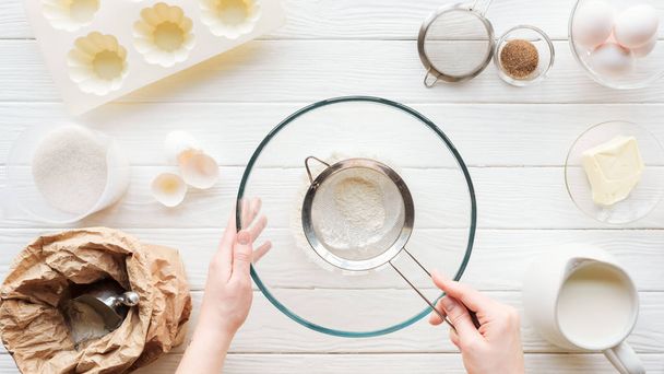 partial view of woman sieving flour in bowl on table with ingredients - Foto, Bild