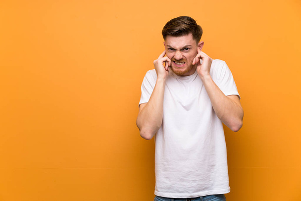 pelirroja hombre sobre marrón pared frustrado y cubriendo orejas
 - Foto, Imagen