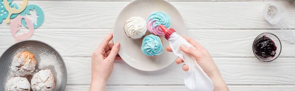panoramic shot of woman decorating cupcakes with icing bag on white table - Photo, Image