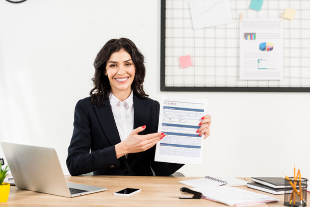attractive and cheerful recruiter holding resume and gesturing in office  - Photo, Image